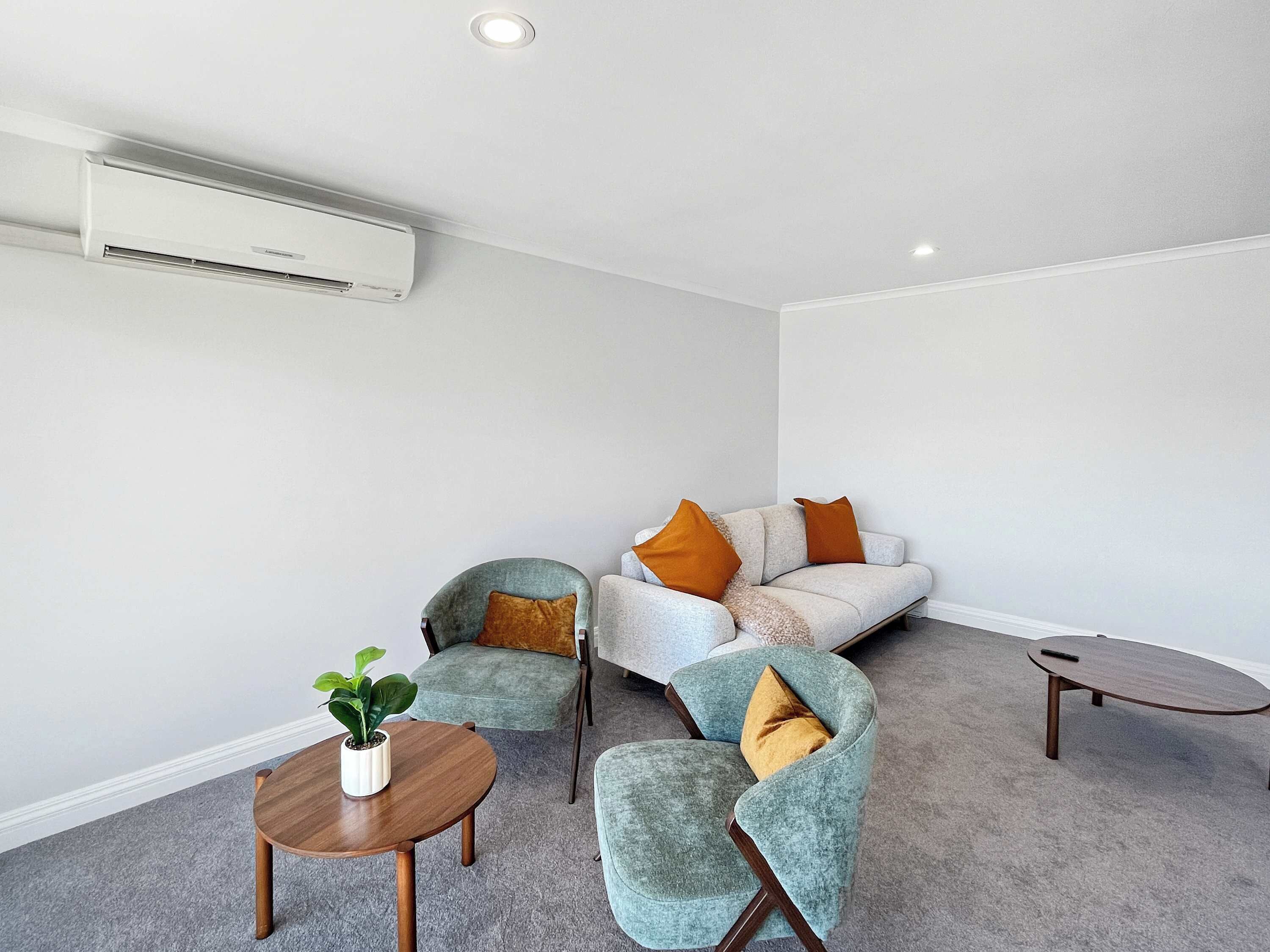 A modern living room with a grey sofa, two armchairs, a small wooden table with a plant, and a round coffee table.