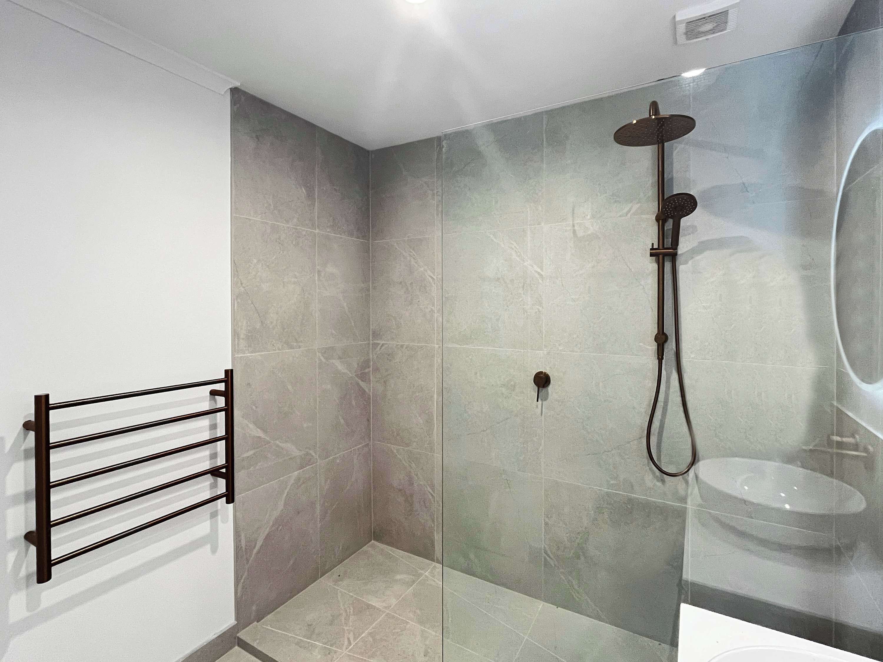 A modern bathroom with a glass shower enclosure, a black towel rack, and a visible sink.