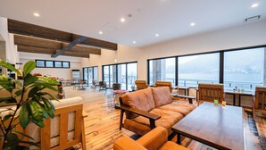 A spacious lounge area with wooden flooring, large windows offering a view of the city, and comfortable seating arrangements. - ZEN RESORT NIKKO (Nikko)