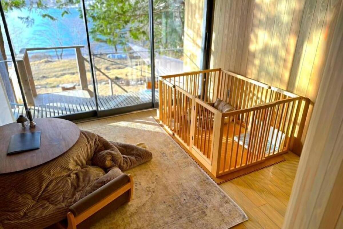 A room with a large window, a wooden crib, a round table, and a patterned rug.