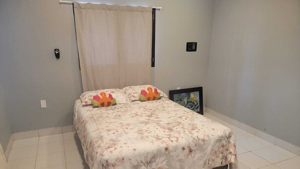 Ein Schlafzimmer mit Bett, Vorhang, Wandleuchte, einem gerahmten Bild und einem Thermostat.
