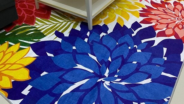 Un soggiorno moderno con un tavolino in vetro, un divano con cuscini colorati, un tappeto dai motivi floreali vivaci e una piccola decorazione a forma di veliero.
