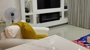 Un soggiorno moderno con una TV a schermo piatto montata su una parete bianca, un divano bianco con una coperta gialla e un'ampia finestra con tende.