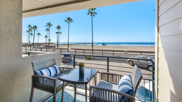Un balcon agrémenté de meubles en osier, d’une table en verre et offrant une vue sur la plage et l’océan.
