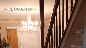 A hallway with a wooden floor, a red patterned rug, a chandelier, and a door with a white frame. - Delightful 2-bedroom house with AC in vibrant Newark (Newark)