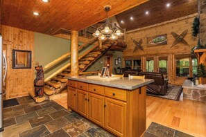 A spacious cabin interior with a wooden staircase, a large wooden dining table, and a cozy fireplace area. - Luxury Lodge in Hocking Hills, 4 Fireplaces, 12-Person Hot Tub, Secret Game Room (Laurelville)
