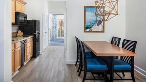 A modern kitchen with wooden cabinets and a black refrigerator, a dining area with a wooden table and blue chairs, and a hanging geometric light fixture. - Harborside at Atlantis – Premium 2-Bedroom Villa with Full Resort Access (N.P)