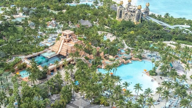 An aerial view of a resort with multiple swimming pools, palm trees, and a large water park structure. - Harborside at Atlantis – Premium 2-Bedroom Villa with Full Resort Access (N.P)
