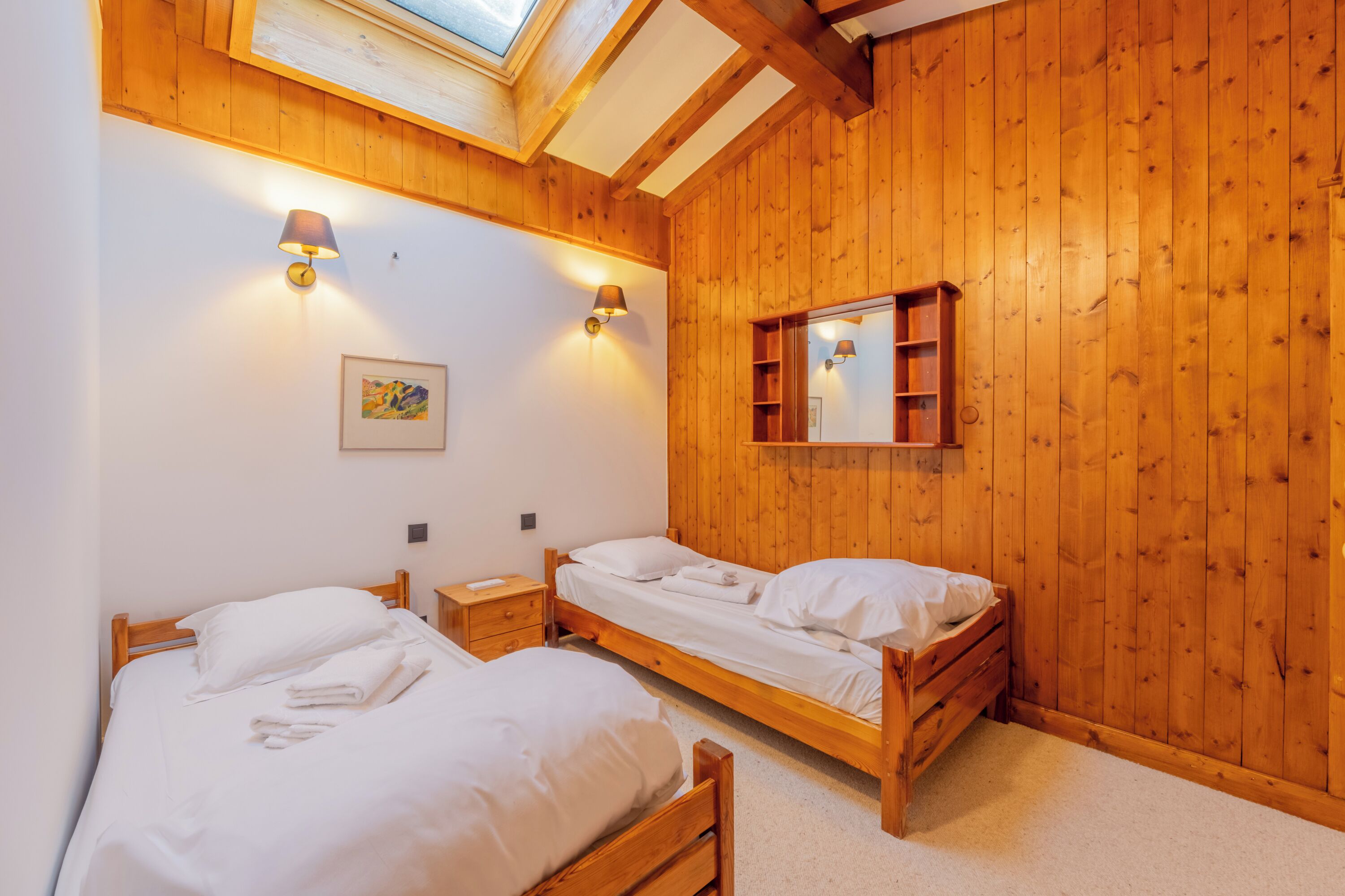 A room with two wooden beds, a skylight, and a wooden wall with a mirror and shelf.