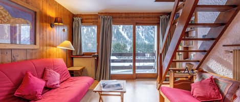 Una habitación acogedora con paredes de madera, un sofá rojo, una mesita y una escalera que lleva a un balcón.