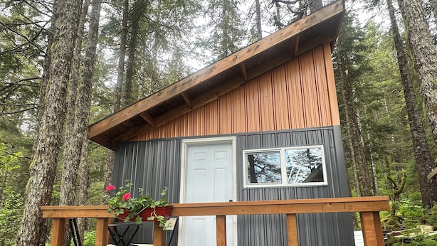 Une petite cabane avec une terrasse en bois, une porte blanche et une fenêtre.