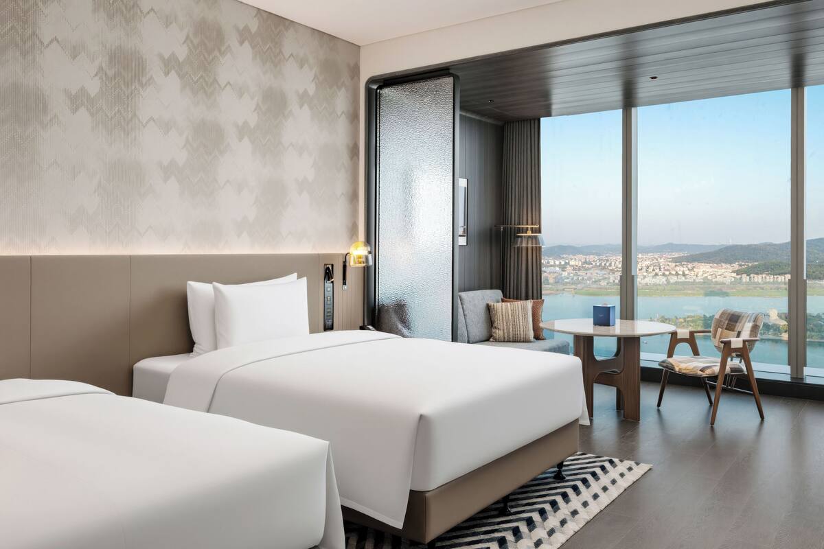 Habitación de hotel con dos camas, vistas a la ciudad y un balcón con mesa y sillas.