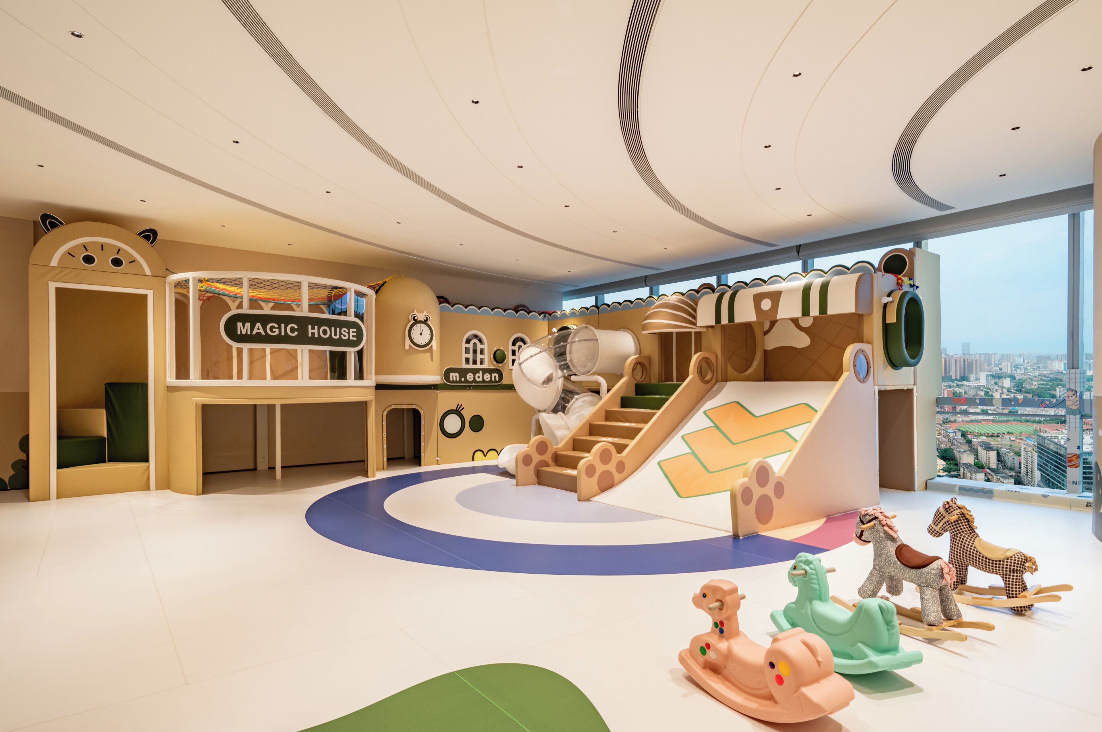 Zona de juegos infantiles con tobogán, pared de escalar y un cartel que dice 'MAGIC HOUSE'.