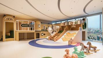 Zona de juegos infantiles con tobogán, pared de escalar y un cartel que dice 'MAGIC HOUSE'.
