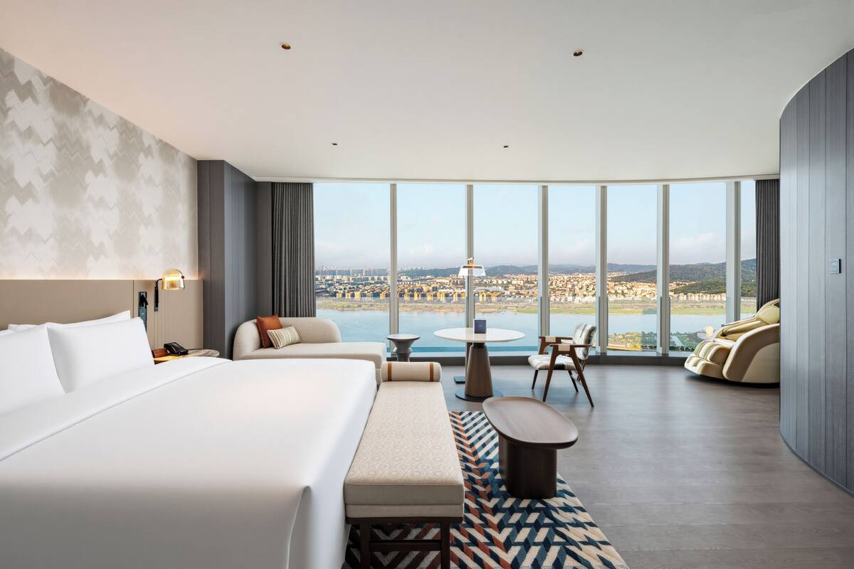Una habitación de hotel con una cama grande, un área de estar con vistas y una mesa de comedor.
