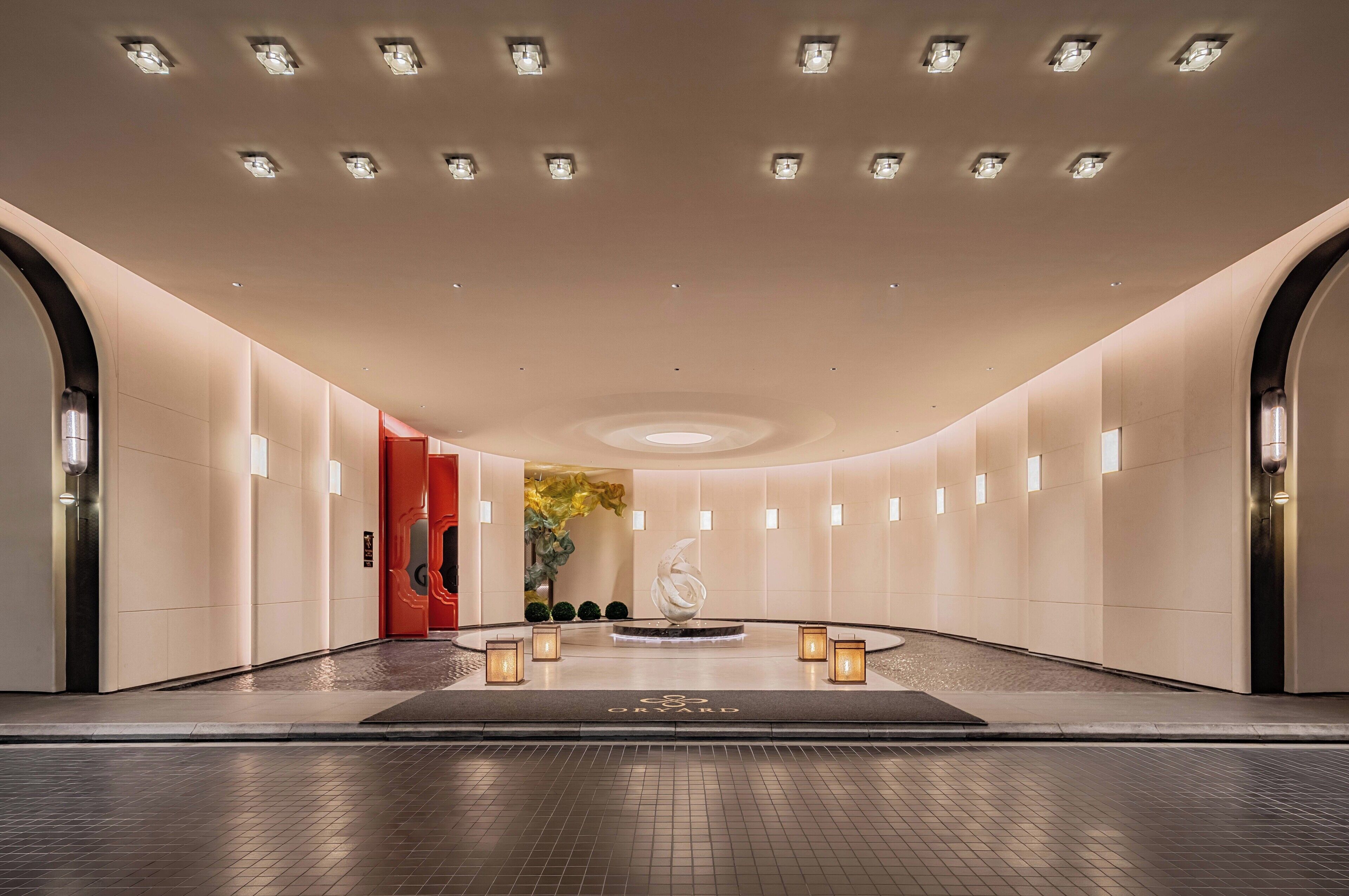 A modern hotel lobby with a central fountain, recessed lighting, and a red accent wall.