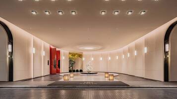 A modern hotel lobby with a central fountain, recessed lighting, and a red accent wall.