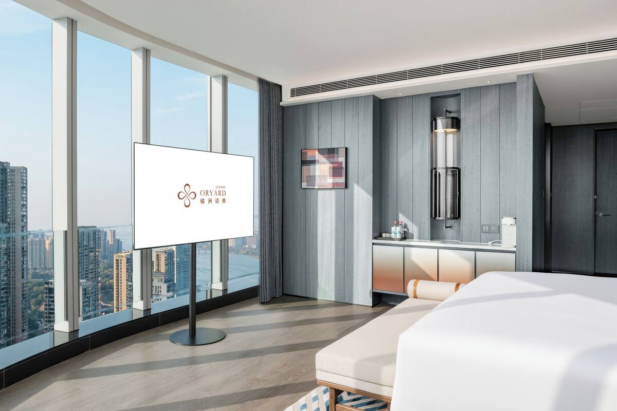 Habitación de hotel moderna con un gran ventanal, cama, escritorio y vistas a la ciudad.