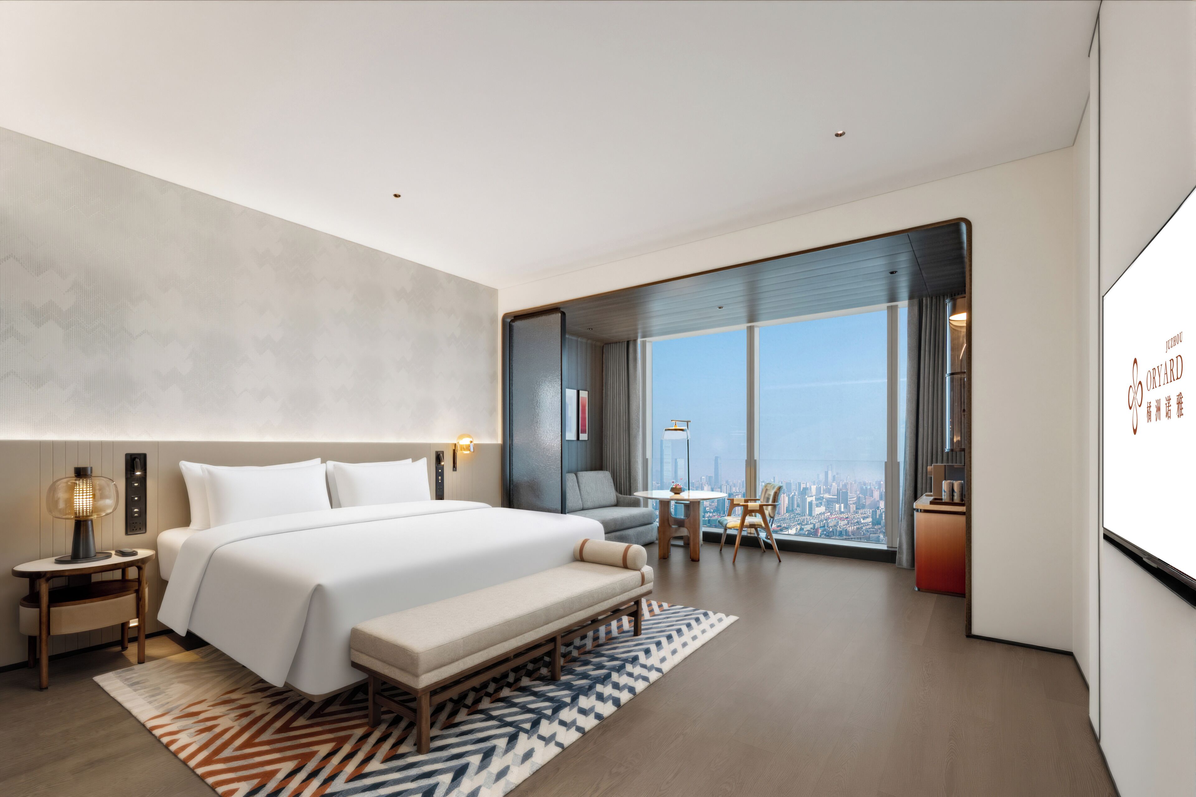 A modern hotel room with a large bed, a seating area, a desk, and a city view.
