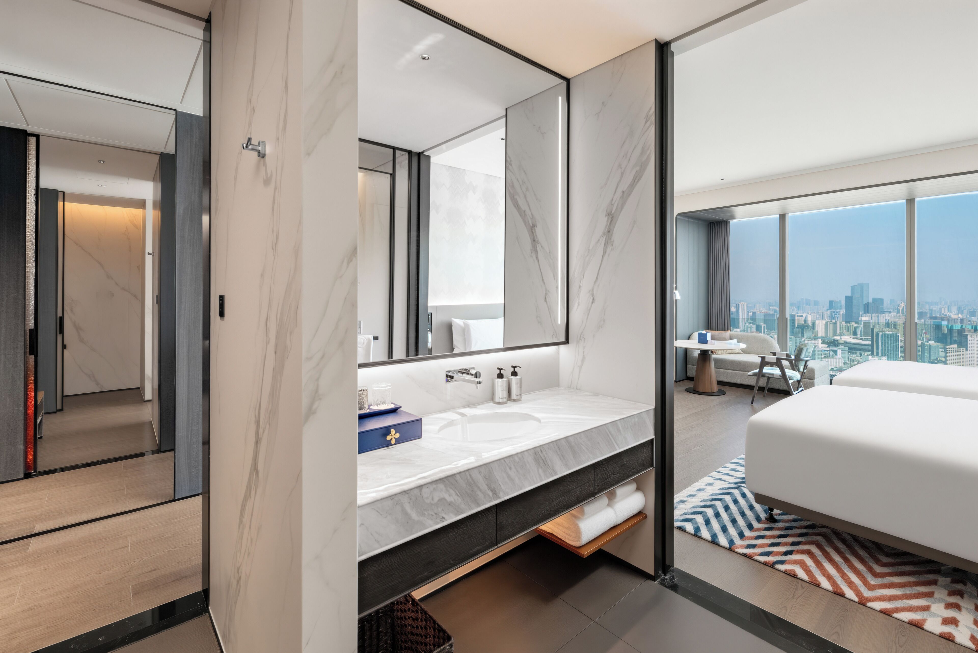Una habitación de hotel moderna con una cama grande, un baño con tocador de mármol y vistas a la ciudad.