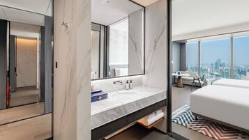 Una habitación de hotel moderna con una cama grande, un baño con tocador de mármol y vistas a la ciudad.