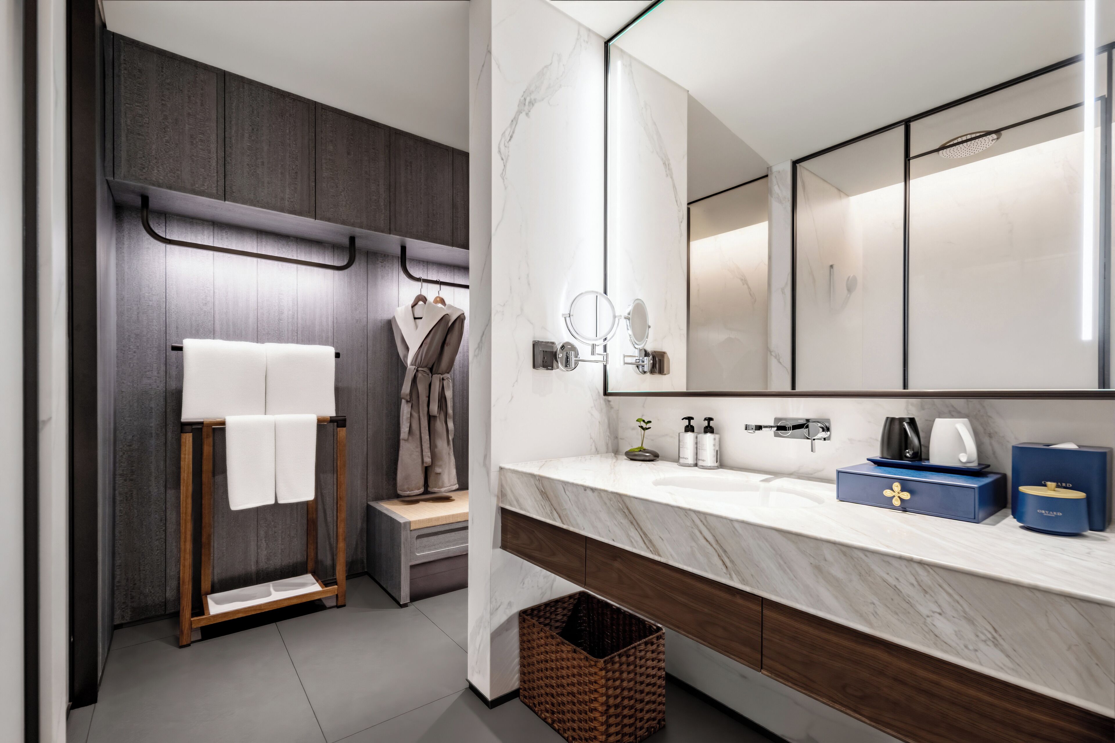 A modern bathroom with a marble vanity, a large mirror, and a wooden towel rack.