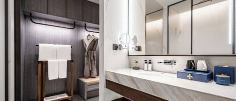 A modern bathroom with a marble vanity, a large mirror, and a wooden towel rack.