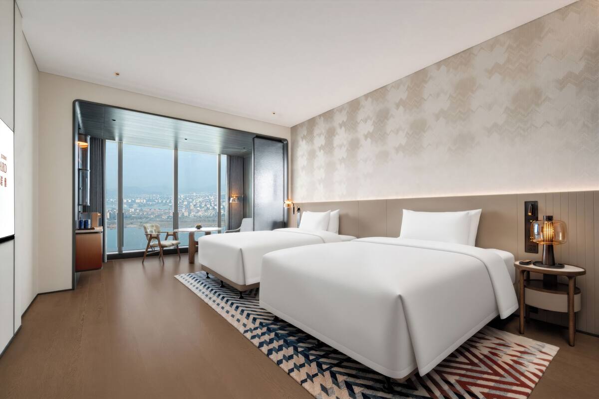 Habitación de hotel moderna con dos camas, vistas a la ciudad y un ventanal grande.