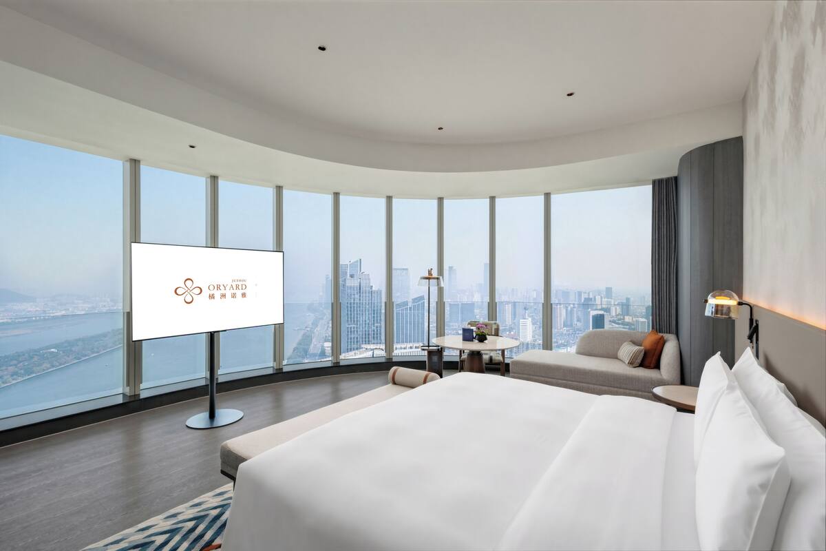 Una habitación de hotel moderna con una cama grande, zona de estar, televisor y vista a la ciudad.
