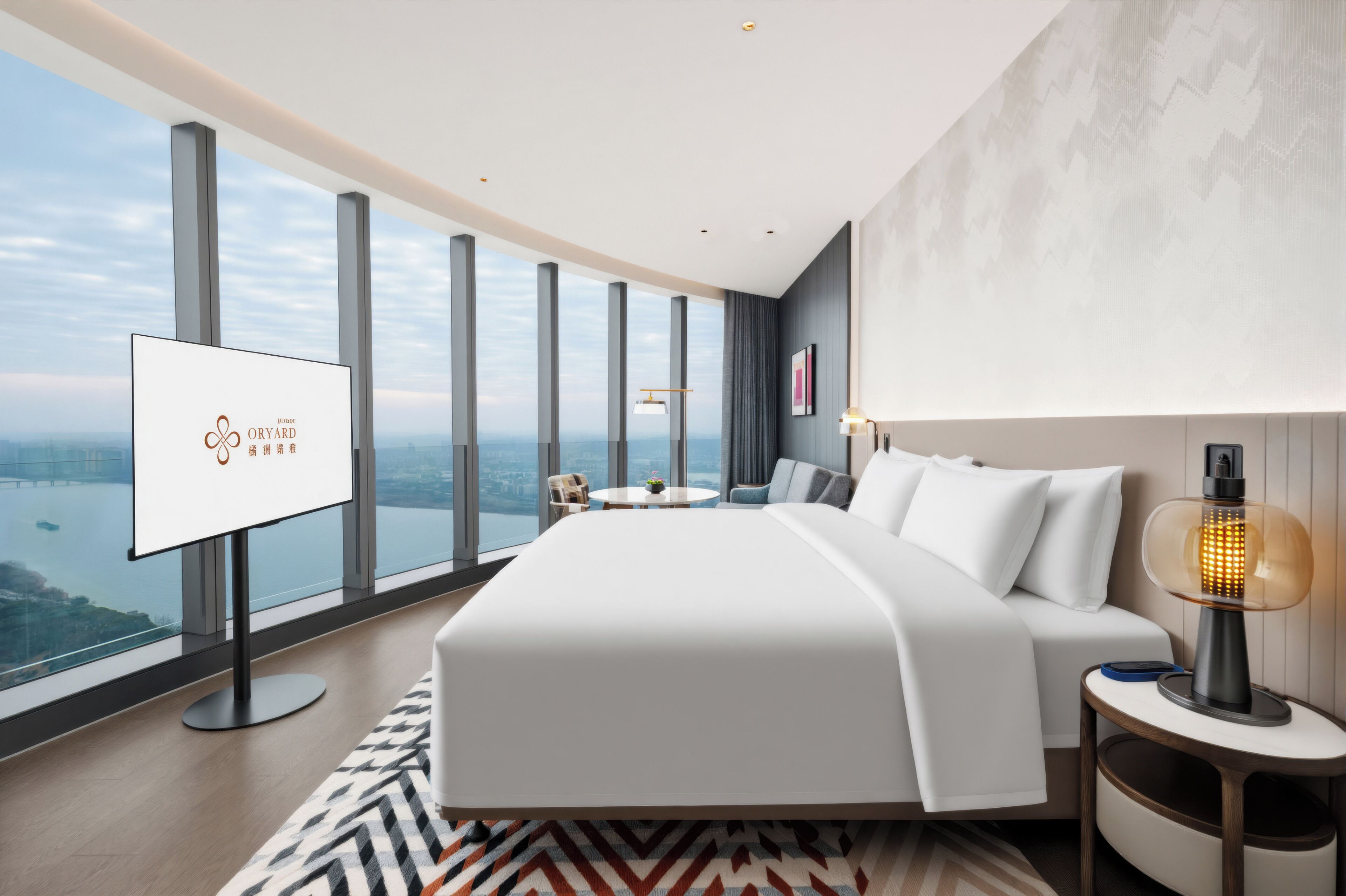 A modern hotel room with a large bed, a TV, a nightstand, and a view of a cityscape.