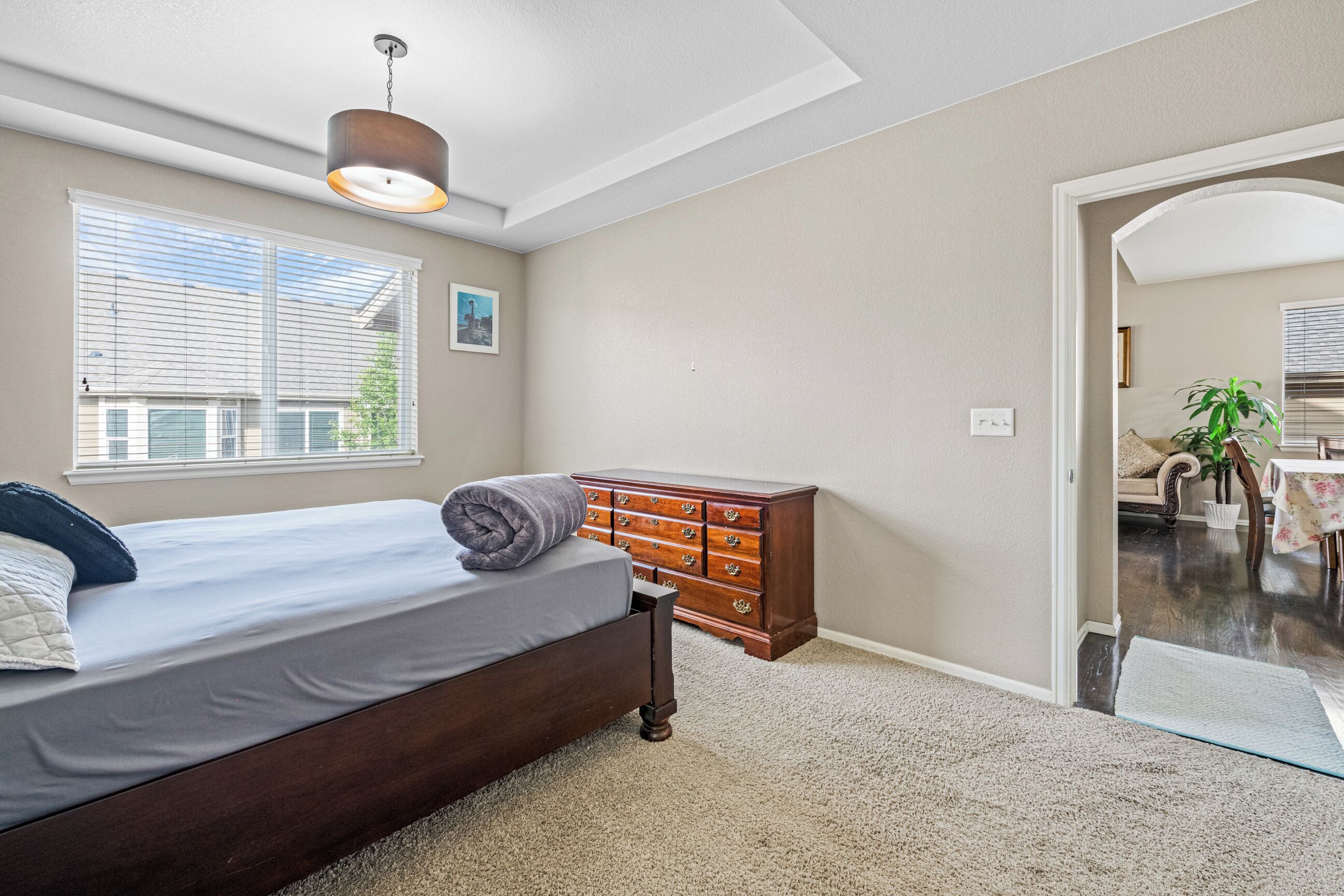 A bedroom with a bed, dresser, and a window with blinds.