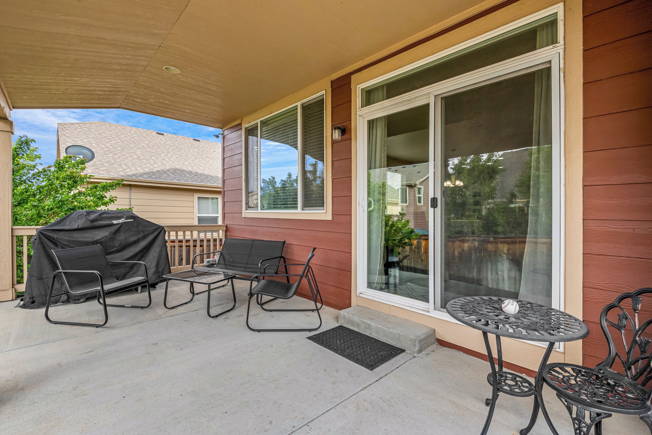 A covered patio with a barbecue grill, two chairs, a table, and a sliding glass door.