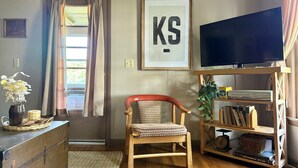 A cozy room with a wooden chair, a television, a bookshelf, and a framed sign on the wall. - Country Farmhouse on a Working Cattle Ranch (El Dorado)