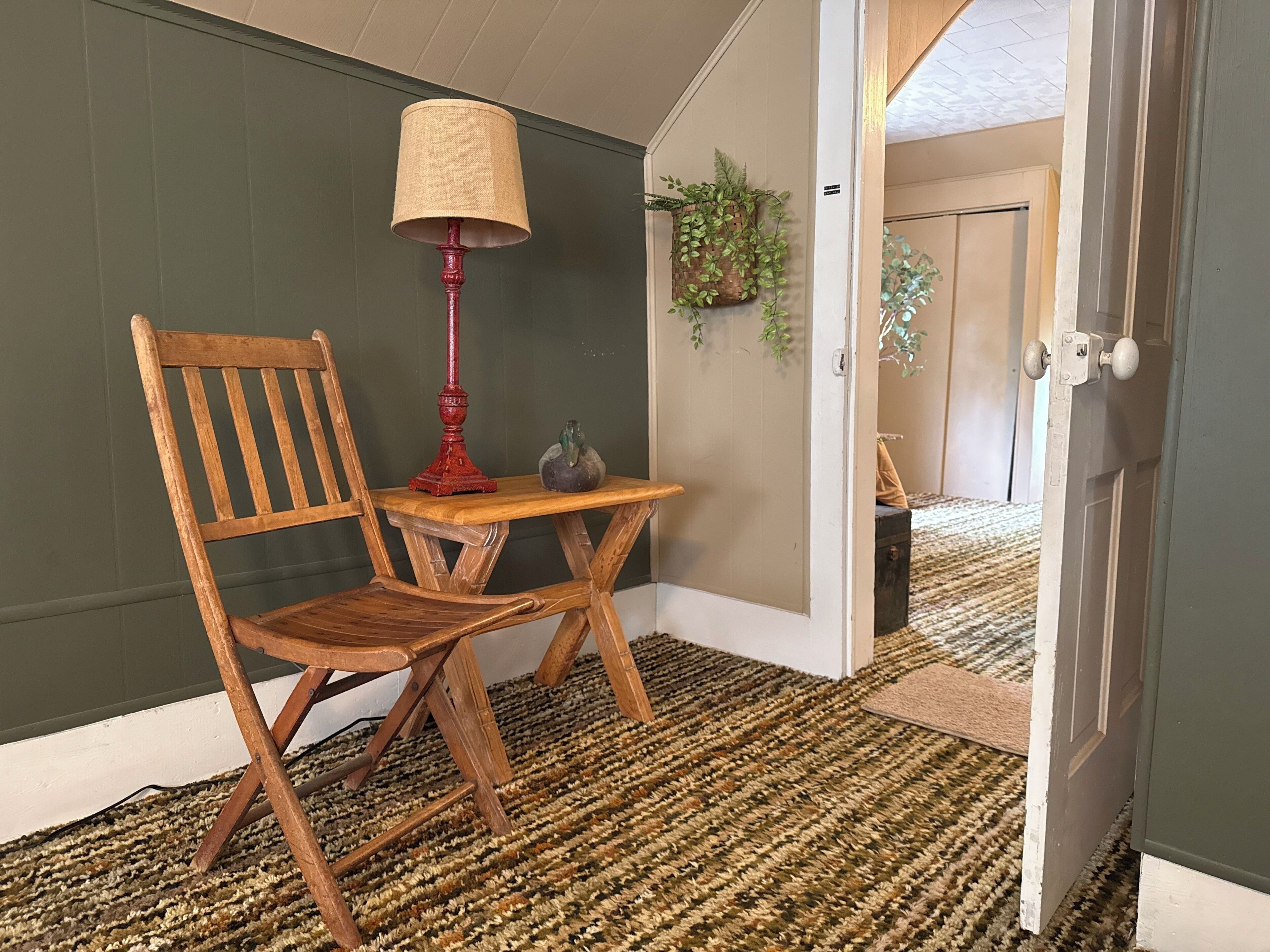 A wooden chair and table in a room with a green wall and a patterned carpet.