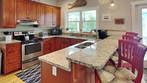 Une cuisine dotée de meubles en bois, de plans de travail en granit, d’appareils électroménagers en acier inoxydable et d’un grand îlot central avec des places assises.