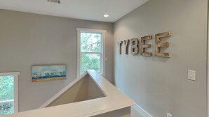 Une pièce avec un plafond blanc, une fenêtre donnant sur des arbres, un tableau accroché au mur et le mot « TYBEE » écrit en grandes lettres.