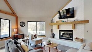 Uma sala de estar com lareira, televisão fixada acima dela e uma janela grande que traz luz natural.