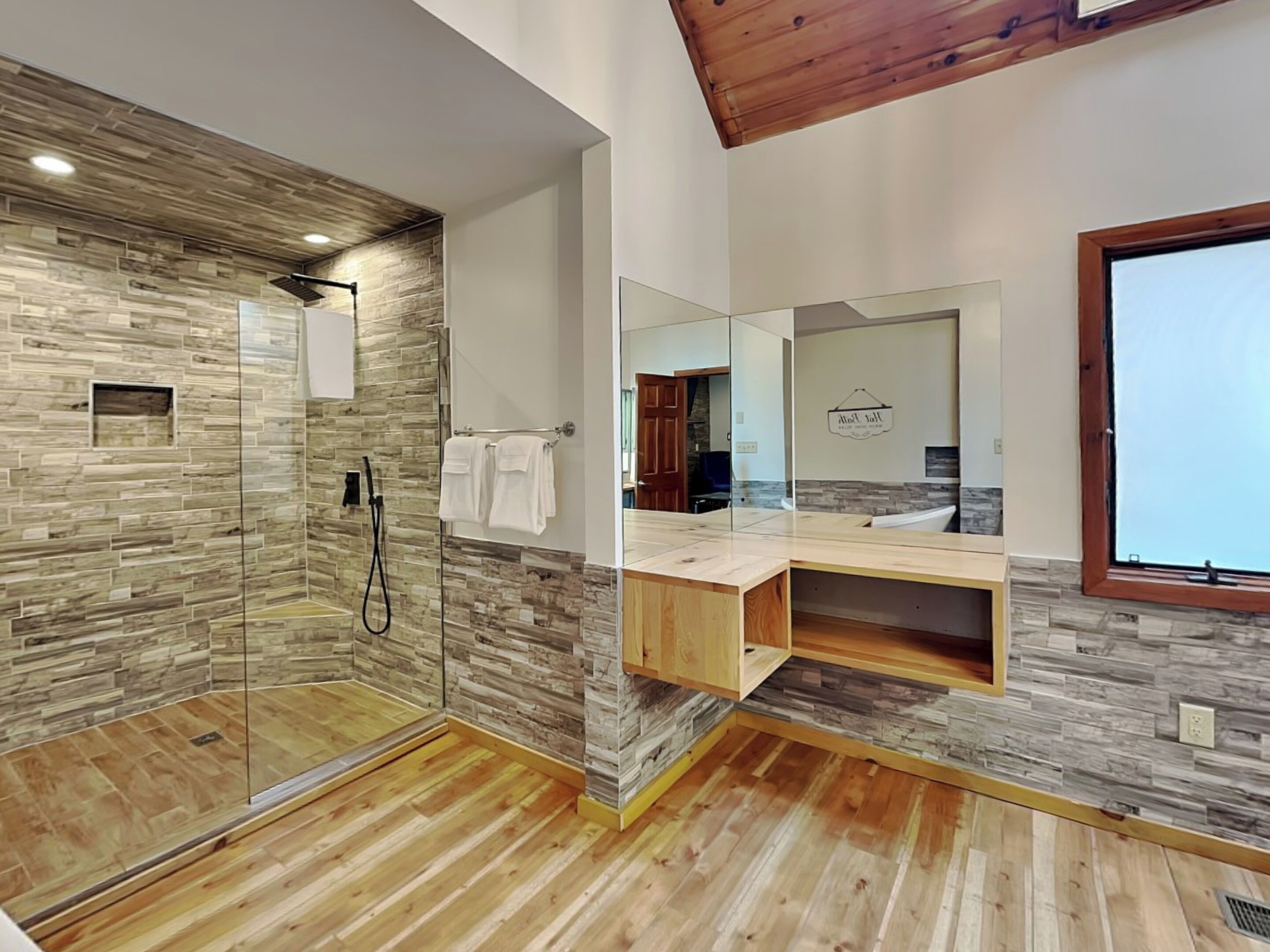 A modern bathroom with a glass shower enclosure, wooden floor, and a vanity with a mirror.