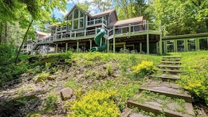 A large, multi-story wooden cabin with a green exterior, surrounded by lush greenery and a winding staircase leading to the entrance. - Copper Canoe (Oakland)