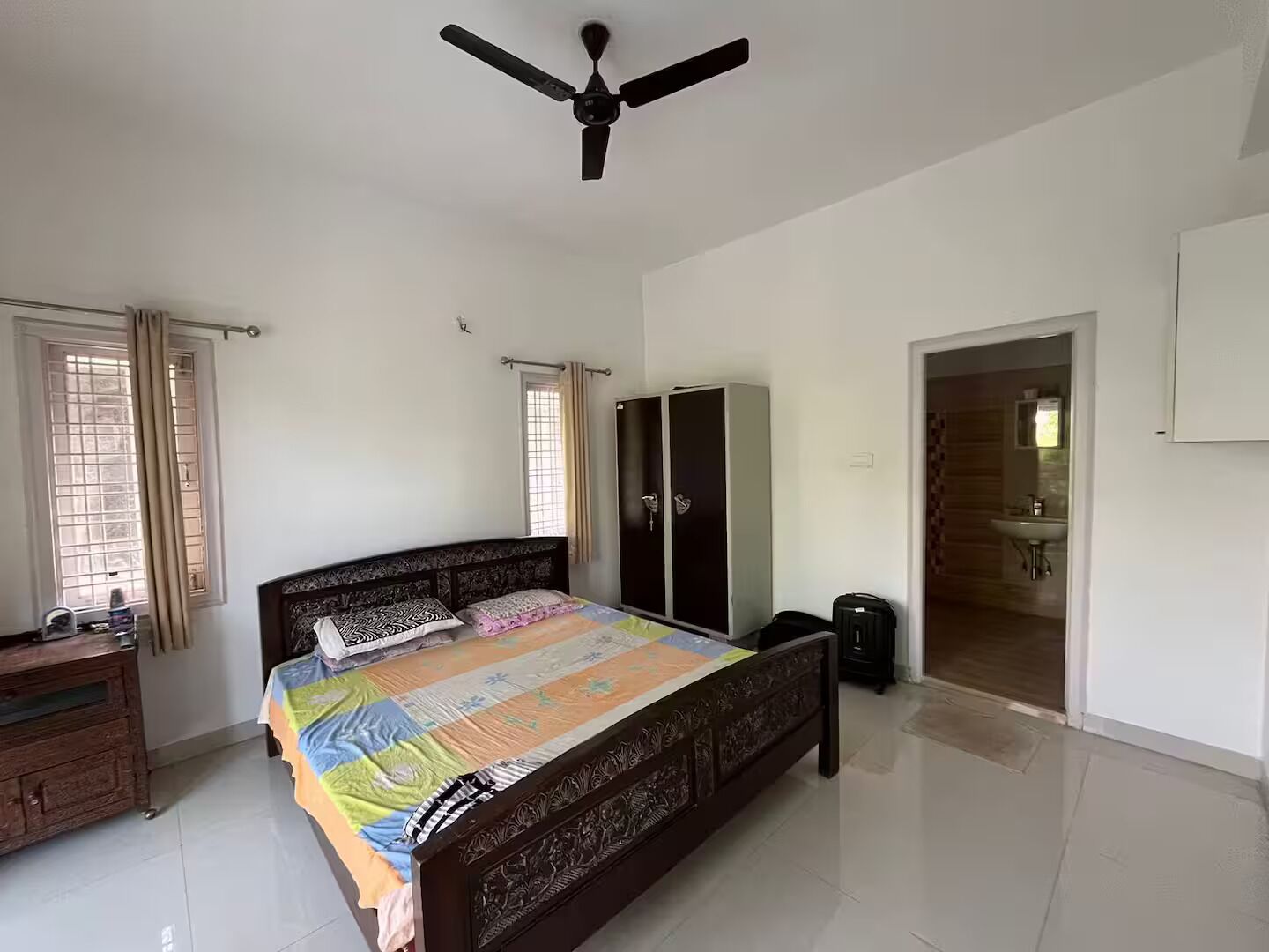 Camera da letto con un letto, armadio, ventilatore a soffitto e bagno visibile attraverso una porta aperta.