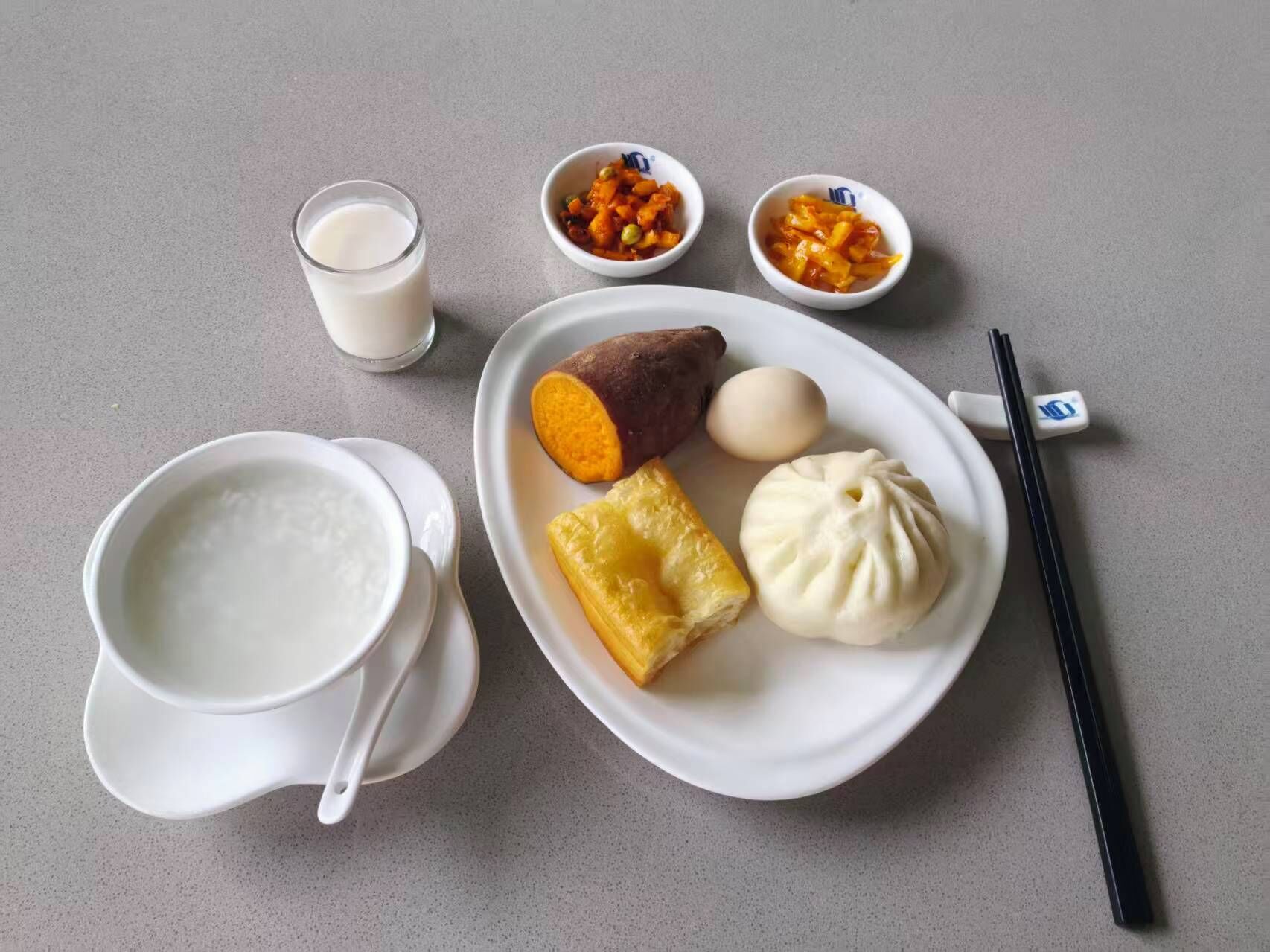A plate with a sweet potato, a dumpling, and a boiled egg, accompanied by a glass of milk and two small bowls of pickled vegetables.