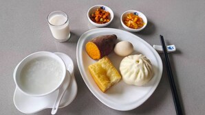 Un plato con boniato, un bollo y un huevo cocido, acompañado de un vaso de leche y dos recipientes pequeños de vegetales encurtidos.