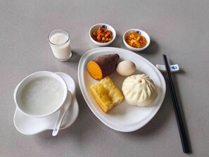 A plate with a sweet potato, a dumpling, and a boiled egg, accompanied by a glass of milk and two small bowls of pickled vegetables. - Timeless Recreation Hotel (Shangrao)
