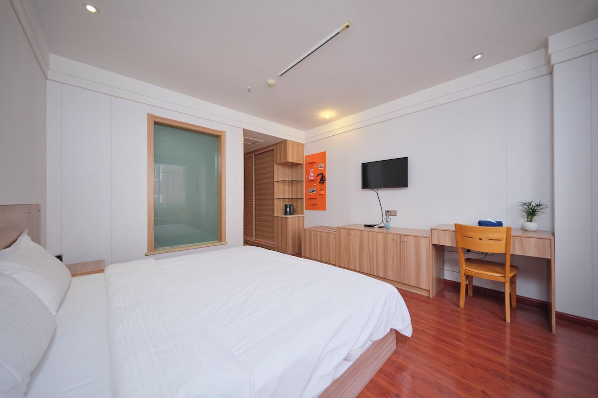A modern bedroom with a large bed, a desk, a chair, and a television.