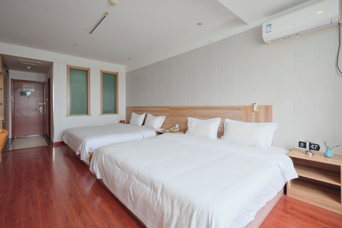 A hotel room with two beds, a wooden headboard, a bedside table with a phone, and a wall-mounted air conditioner.