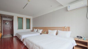 Hotellihuone, jossa on kaksi sänkyä, puinen pääty, yöpöytä, jossa on puhelin, ja seinälle asennettu ilmastointilaite.