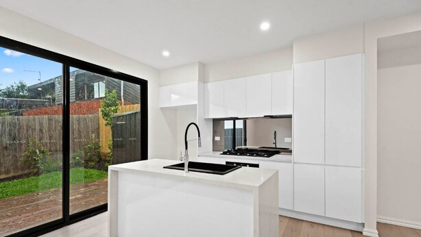 A modern kitchen with white cabinetry, a central island with a sink, and a large sliding glass door to the outside. - French home walking to shops and shopping center (Maidstone)