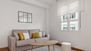 Ein modernes Wohnzimmer mit grauem Sofa, einem Holztisch und einem weißen Hocker.