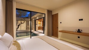 Une chambre d’hôtel moderne dotée d’un grand lit, d’une table de chevet en bois, d’un balcon fermé par des baies vitrées et offrant une vue sur l’espace extérieur.
