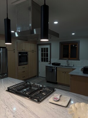 A modern kitchen with a gas stove, stainless steel appliances, wooden cabinets, and pendant lighting. - Private Modern Adirondack Home (Saranac Lake)